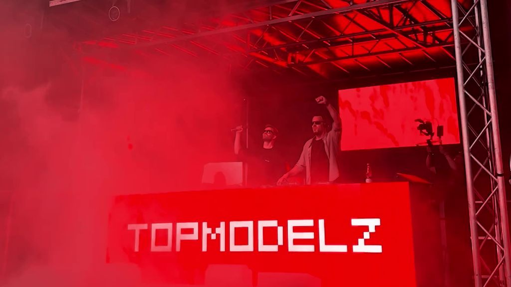 Topmodelz on stage in red light behind the Topmodelz DJ booth